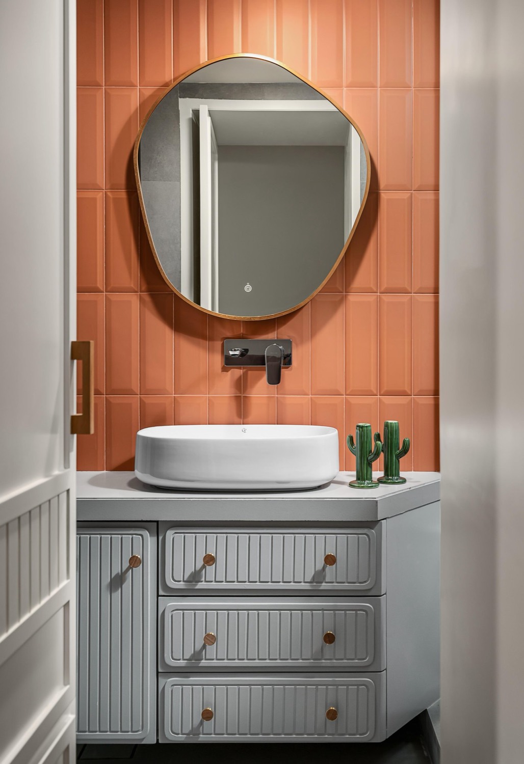 Terracotta tiled powder room with organic-shaped mirror and fluted vanity